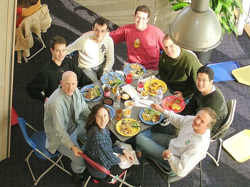 A group of 8 smiling people (one of whom is Ellen Spertus) sitting around a Google cafeteria table